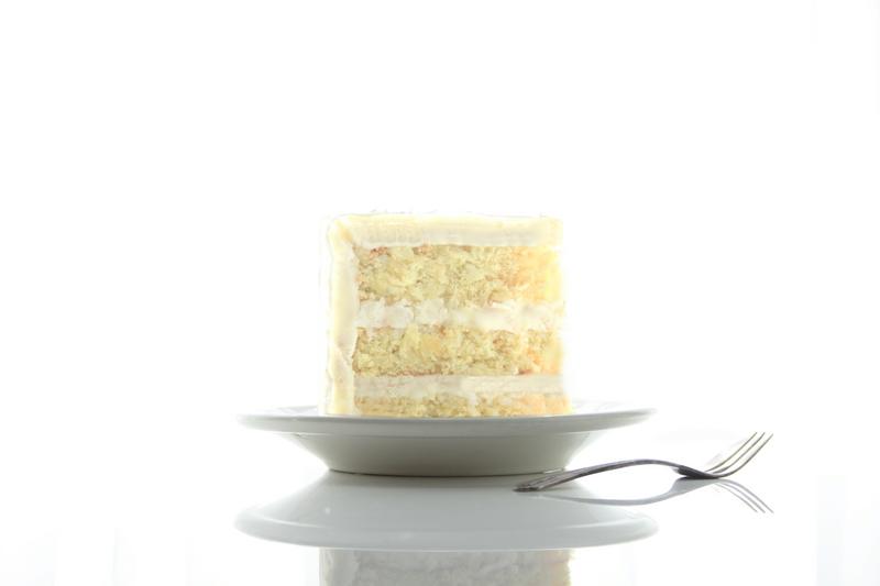 Tall slice of Savannah Coconut Cake on white plate with spoon