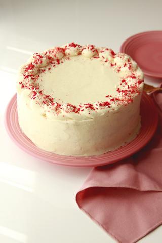 Whole streamlined red velvet cake on a stand with pink cloth
